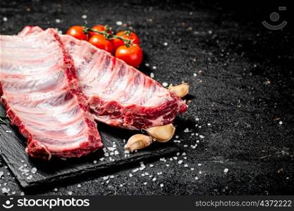 Raw ribs on a stone board with tomatoes and pieces of salt. On a black background. High quality photo. Raw ribs on a stone board with tomatoes and pieces of salt.