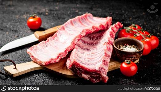 Raw ribs on a wooden cutting board with spices and tomatoes. On a black background. High quality photo. Raw ribs on a wooden cutting board with spices and tomatoes.