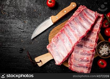 Raw ribs on a wooden cutting board with spices and tomatoes. On a black background. High quality photo. Raw ribs on a wooden cutting board with spices and tomatoes.