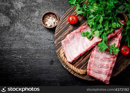 Raw ribs with greenery on a wooden tray. On a black background. High quality photo. Raw ribs with greenery on a wooden tray.