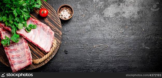 Raw ribs with greenery on a wooden tray. On a black background. High quality photo. Raw ribs with greenery on a wooden tray.
