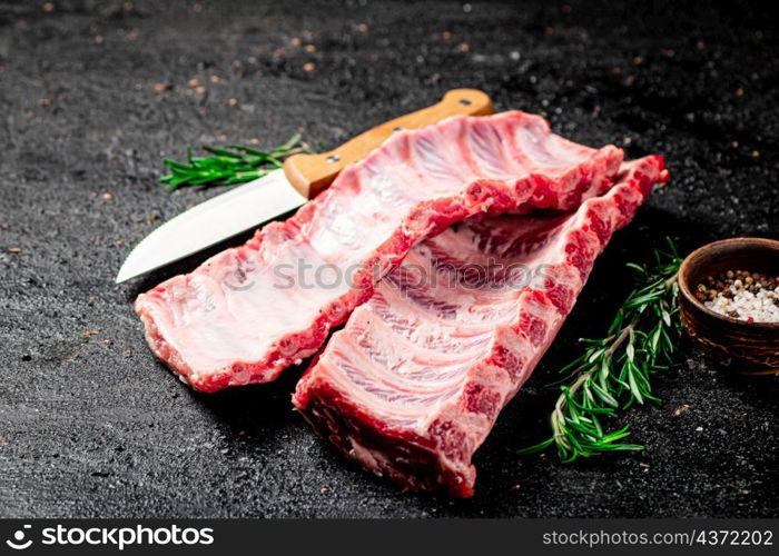 Raw ribs with rosemary and knife. On a black background. High quality photo. Raw ribs with rosemary and knife.