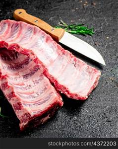 Raw ribs with rosemary and knife. On a black background. High quality photo. Raw ribs with rosemary and knife.