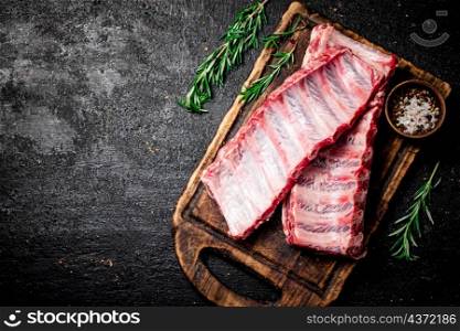 Raw ribs with rosemary and spices on a cutting board. On a black background. High quality photo. Raw ribs with rosemary and spices on a cutting board.