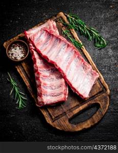 Raw ribs with rosemary and spices on a cutting board. On a black background. High quality photo. Raw ribs with rosemary and spices on a cutting board.