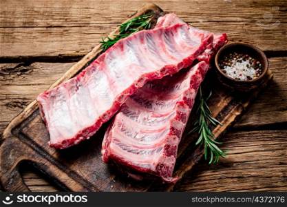 Raw ribs with spices and rosemary on a cutting board. On a wooden background. High quality photo. Raw ribs with spices and rosemary on a cutting board.