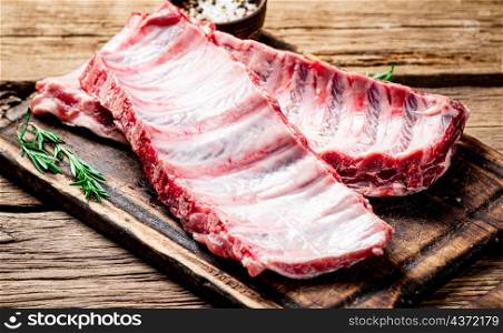 Raw ribs with spices and rosemary on a cutting board. On a wooden background. High quality photo. Raw ribs with spices and rosemary on a cutting board.