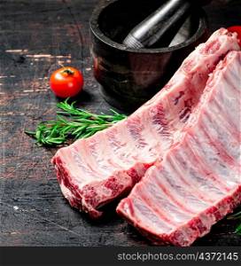 Raw ribs with spices and tomatoes on the table. On a rustic dark background. High quality photo. Raw ribs with spices and tomatoes on the table.