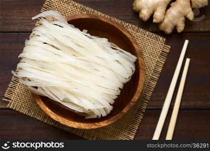 Raw rice flour noodles in wooden bowl, photographed overhead on dark wood with natural light (Selective Focus, Focus on the top of the noodles)