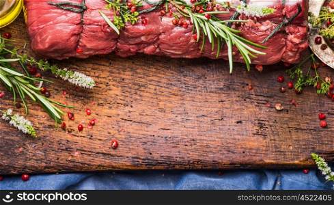 Raw roast beef with herbs and spices tied with a rope on wooden background, top view, border