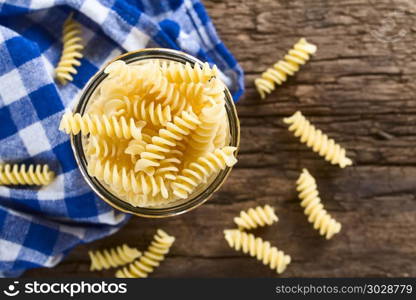 Raw rotini or fusilli pasta in glass jar, photographed overhead on rustic wood (Selective Focus, Focus on the top rotinis). Raw Rotini or Fusilli Pasta
