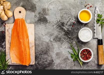 Raw salmon filet on marble board, knife and spices over grey stone background, wild atlantic fish, top view, flat lay. Raw salmon filet and ingredients, flat lay, top view