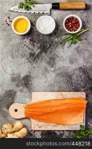 Raw salmon filet on marble board, knife and spices over grey stone background, wild atlantic fish, top view, flat lay. Raw salmon filet and ingredients, flat lay, top view