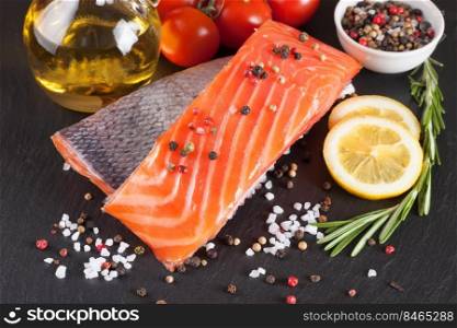 Raw salmon fillet and ingredients for cooking on a dark slate background.. Raw salmon fillet