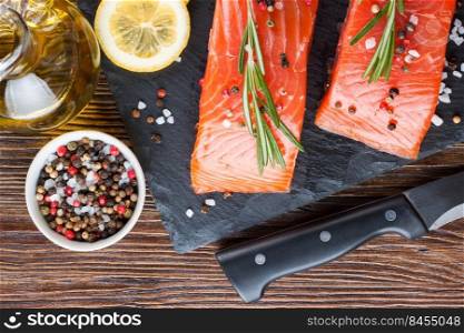 Raw salmon fillet and ingredients for cooking on a slade board and knife on brown wooden background.. Raw salmon fillet with spices