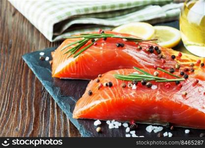 Raw salmon fillet and ingredients for cooking on a slade board and brown wooden background.. Raw salmon fillet with spices
