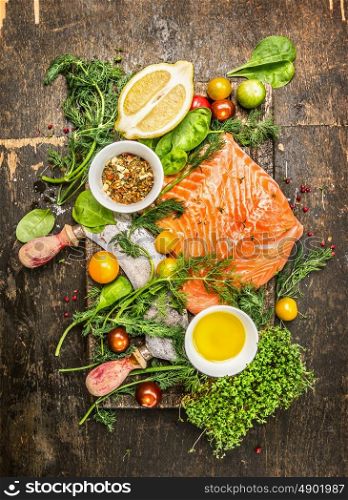 Raw salmon fillet with fresh healthy herbs,vegetables, oil and spices on rustic wooden background, top view