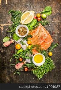 Raw salmon fillet with fresh healthy herbs,vegetables, oil and spices on rustic wooden background, top view