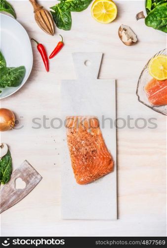 Raw Salmon fillets on white cutting board with healthy ingredients on kitchen table background, top view. Diet nutrition and healthy food concept