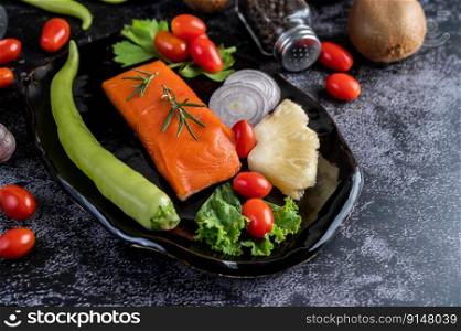 Raw salmon fillets, pepper, kiwi, pineapples, and rosemary onto a plate and black cement floor.