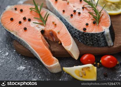 Raw salmon fish fillet and ice for cooked steak seafood / Fresh salmon steak with herbs and spices lemon rosemary tomato on wooden cutting board background
