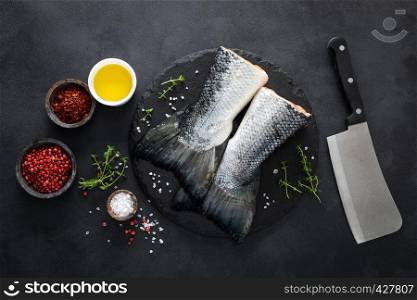 Raw salmon fishtails with ingredients for cooking on black background, top view