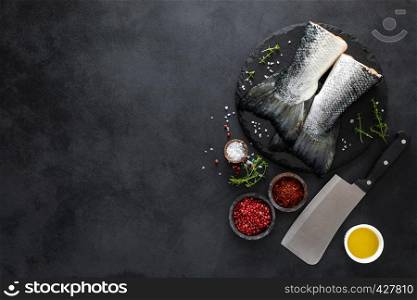 Raw salmon fishtails with ingredients for cooking on black background, top view