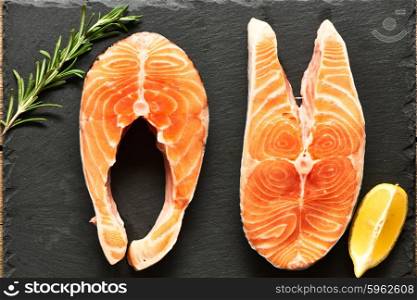 Raw salmon steaks and ingredients on slate background