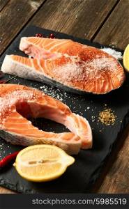 Raw salmon steaks and ingredients on slate background