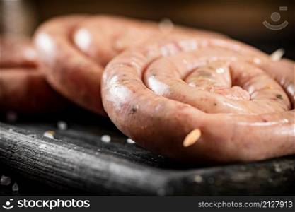 Raw sausage for frying on the table. Against a dark background. High quality photo. Raw sausage for frying on the table.