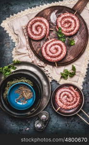Raw sausage on vintage cutting board with herbs and spices, preparation on dark rustic kitchen table, top view