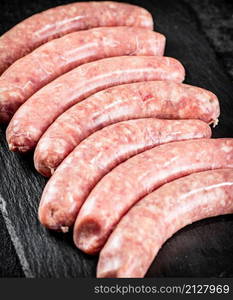 Raw sausages made of fresh meat on a stone board. On a black background. High quality photo. Raw sausages made of fresh meat on a stone board.