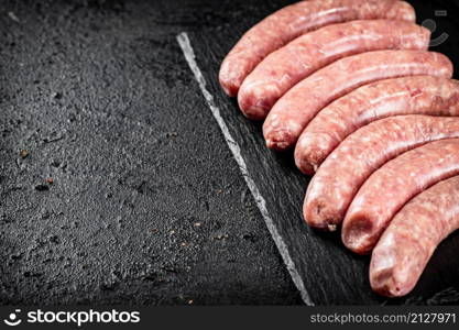 Raw sausages made of fresh meat on a stone board. On a black background. High quality photo. Raw sausages made of fresh meat on a stone board.