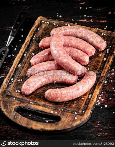 Raw sausages on a cutting board. On a rustic dark background. High quality photo. Raw sausages on a cutting board.