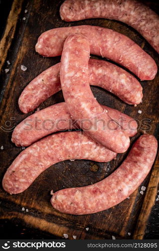 Raw sausages on a cutting board. On a rustic dark background. High quality photo. Raw sausages on a cutting board.