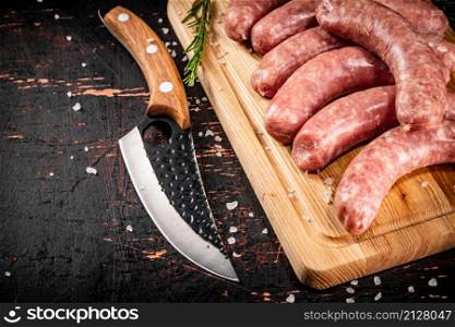 Raw sausages on a cutting board with a knife and rosemary. Against a dark background. High quality photo. Raw sausages on a cutting board with a knife and rosemary.
