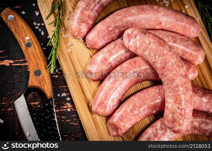 Raw sausages on a cutting board with a knife and rosemary. Against a dark background. High quality photo. Raw sausages on a cutting board with a knife and rosemary.