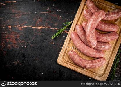 Raw sausages on a cutting board with a sprig of rosemary. On a rustic dark background. High quality photo. Raw sausages on a cutting board with a sprig of rosemary.