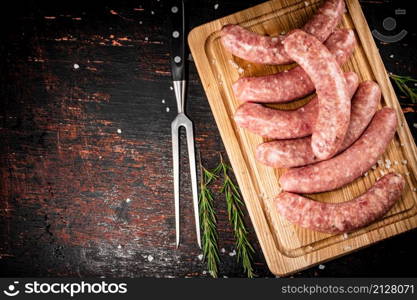 Raw sausages on a cutting board with a sprig of rosemary. On a rustic dark background. High quality photo. Raw sausages on a cutting board with a sprig of rosemary.