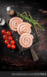 Raw sausages on a cutting board with a sprig of rosemary and tomatoes. On a rustic dark background. High quality photo. Raw sausages on a cutting board with a sprig of rosemary and tomatoes.