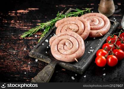 Raw sausages on a cutting board with a sprig of rosemary and tomatoes. On a rustic dark background. High quality photo. Raw sausages on a cutting board with a sprig of rosemary and tomatoes.