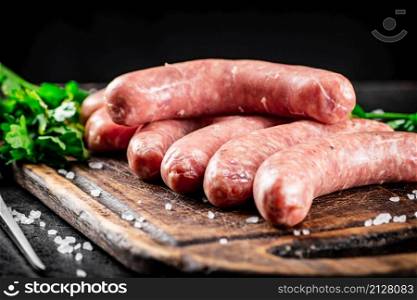 Raw sausages on a cutting board with parsley. On a black background. High quality photo. Raw sausages on a cutting board with parsley.