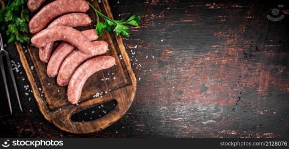 Raw sausages on a cutting board with parsley. On a rustic dark background. High quality photo. Raw sausages on a cutting board with parsley.