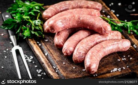 Raw sausages on a cutting board with parsley. On a rustic dark background. High quality photo. Raw sausages on a cutting board with parsley.