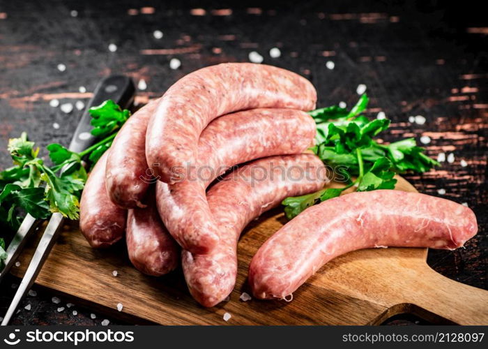 Raw sausages on a cutting board with parsley. On a rustic dark background. High quality photo. Raw sausages on a cutting board with parsley.