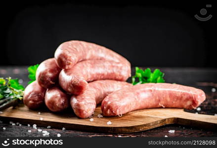 Raw sausages on a cutting board with parsley. On a rustic dark background. High quality photo. Raw sausages on a cutting board with parsley.