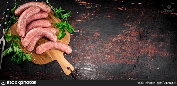 Raw sausages on a cutting board with parsley. On a rustic dark background. High quality photo. Raw sausages on a cutting board with parsley.
