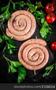 Raw sausages on a stone board with parsley and tomatoes. On a black background. High quality photo. Raw sausages on a stone board with parsley and tomatoes.