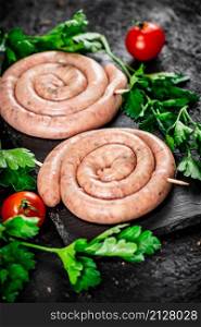 Raw sausages on a stone board with parsley and tomatoes. On a black background. High quality photo. Raw sausages on a stone board with parsley and tomatoes.