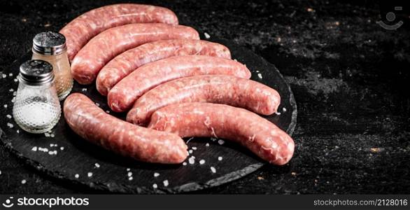 Raw sausages on a stone board with spices. On a black background. High quality photo. Raw sausages on a stone board with spices.